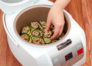 Ang isang kamay ay naglalagay ng pinalamanan na zucchini sa isang mangkok ng multicooker