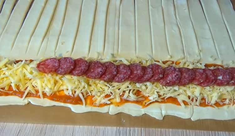 Upang makagawa ng puff pastry pizza, ilagay ang sarsa at punan ang kuwarta