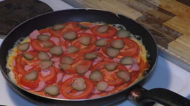 Upang makagawa ng pizza sa isang kawali, ilagay ang mga pipino sa sarsa