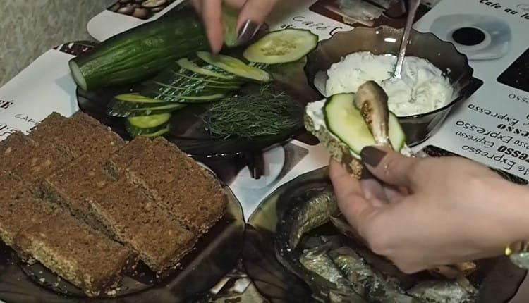 Ikalat ang isang hiwa ng tinapay na may sarsa, maglagay ng isang bilog ng pipino at sprat.